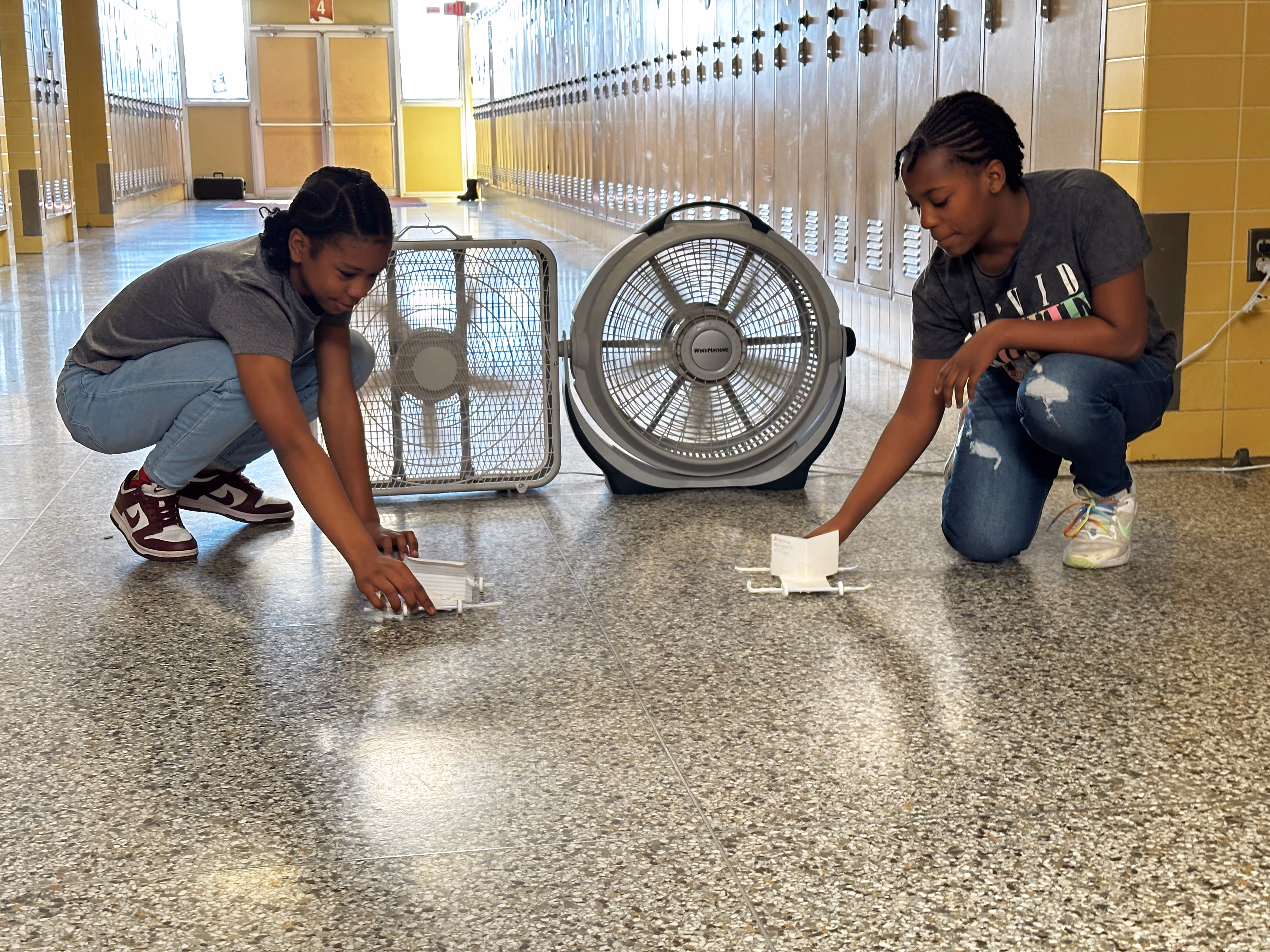 Two students testing wind-powered cars with fans.