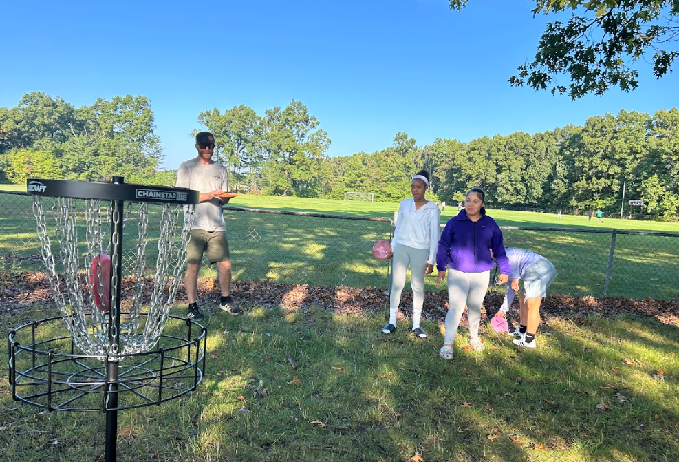 Students practicing playing disc golf toward a basket.